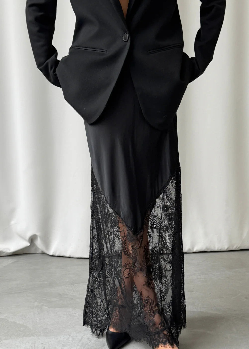 Black suit with a lace-trimmed dress underneath on a neutral background
