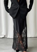 Black suit with a lace-trimmed dress underneath on a neutral background