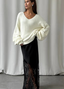 Woman wearing a white sweater and black lace skirt against a grey curtain background