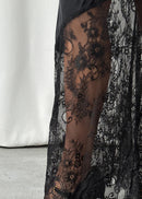 Black lace stockings with floral patterns worn by a person, paired with black shoes on a neutral background.