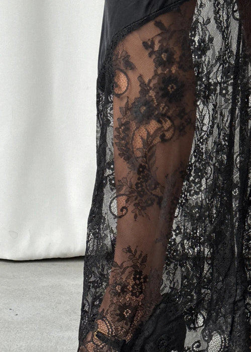 Black lace stockings with floral patterns worn by a person, paired with black shoes on a neutral background.