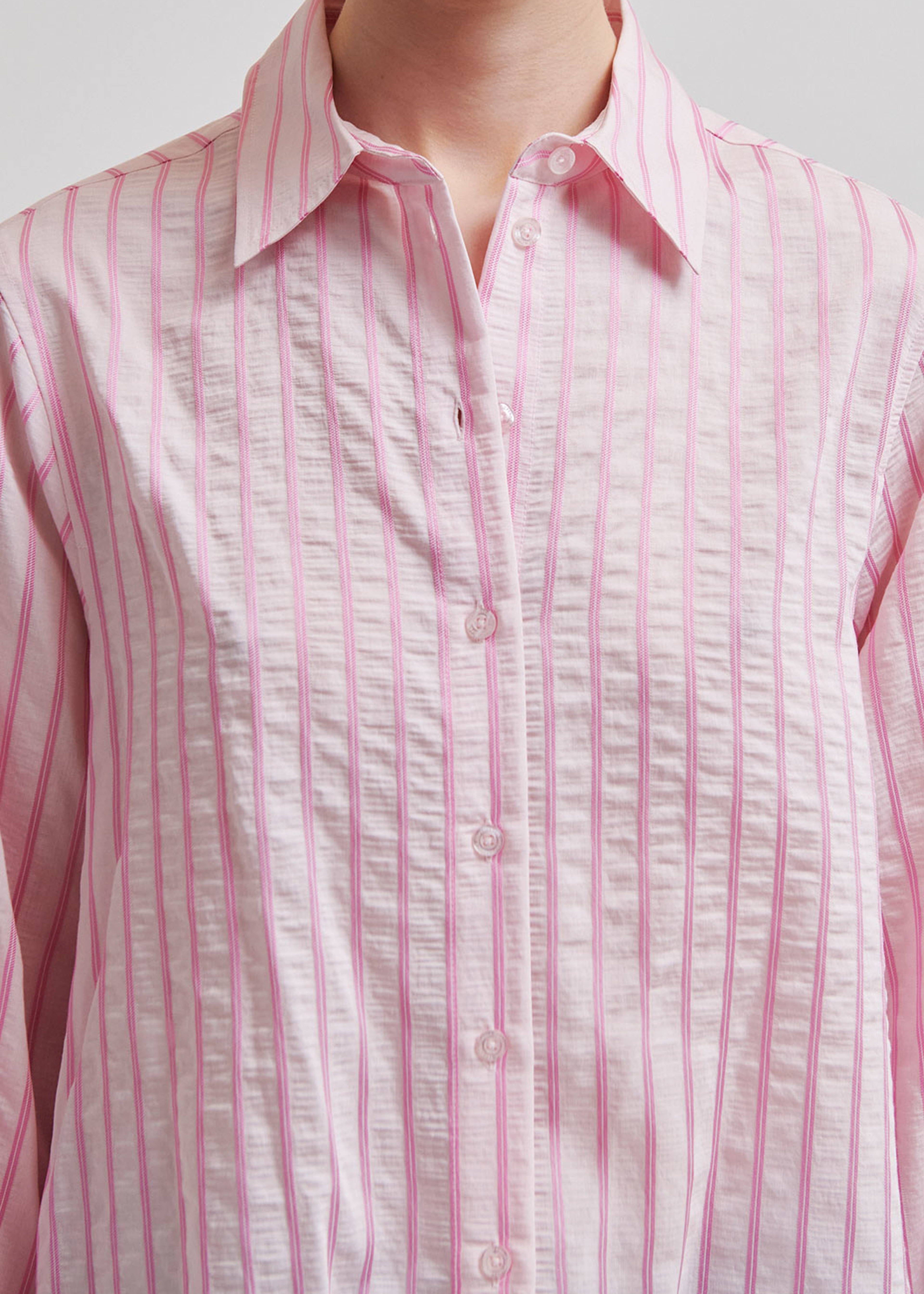 Woman wearing a pink  shirt with blue jeans on a light grey background