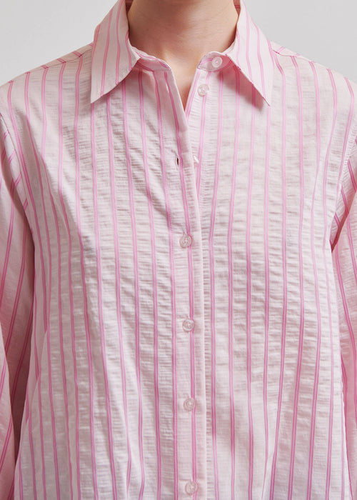 Woman wearing a pink  shirt with blue jeans on a light grey background