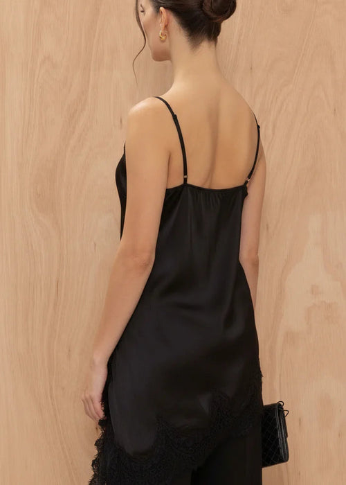 Woman wearing a black satin slip dress with lace trim against a wooden background