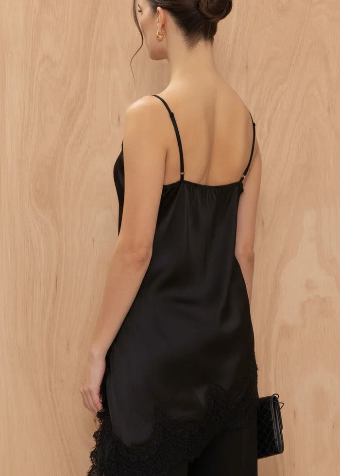Woman wearing a black satin slip dress with lace trim against a wooden background