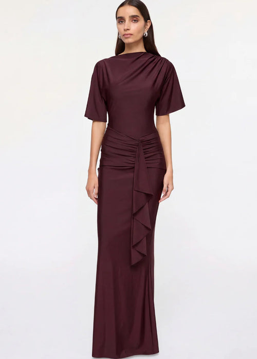 Woman wearing a burgundy evening gown with ruffled details on a white background