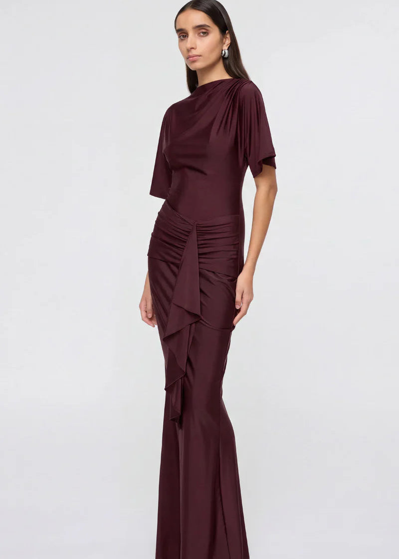 Woman wearing a burgundy evening gown with ruffled details on a white background