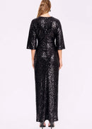 A woman modelling a floor-length black sequined gown with elbow-length flared sleeves, photographed against a plain light background.