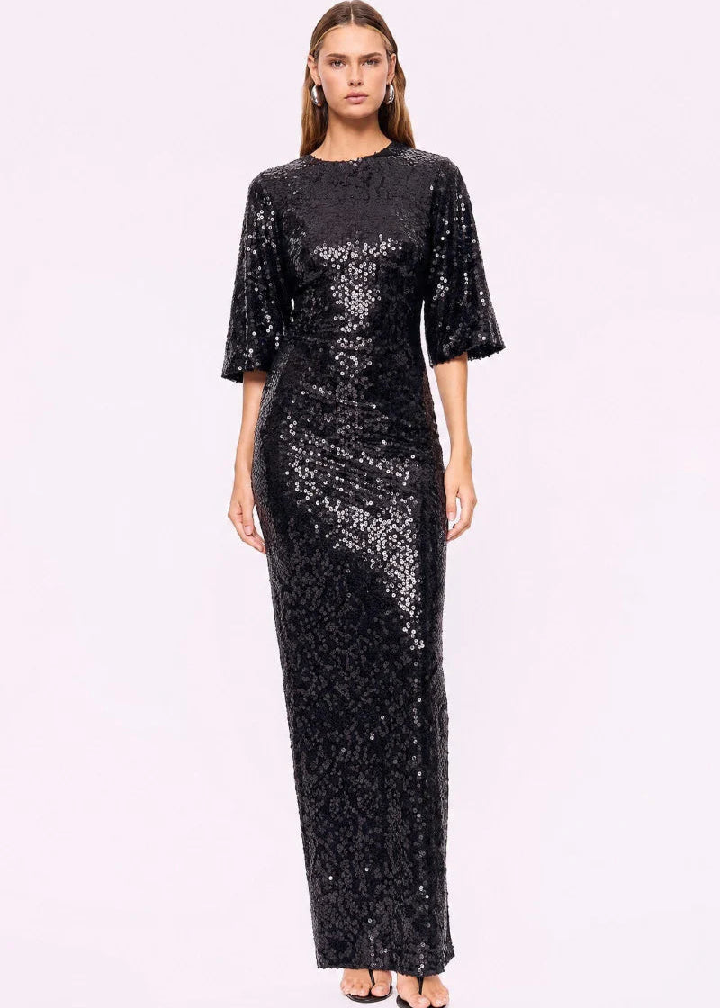 A woman modelling a floor-length black sequined gown with elbow-length flared sleeves, photographed against a plain light background.