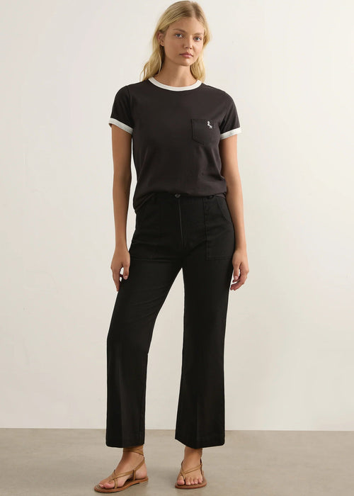A blonde woman modelling a black ringer T-shirt with white trim on the crew neck and sleeve cuffs, featuring a left chest pocket with a small white embroidered logo.