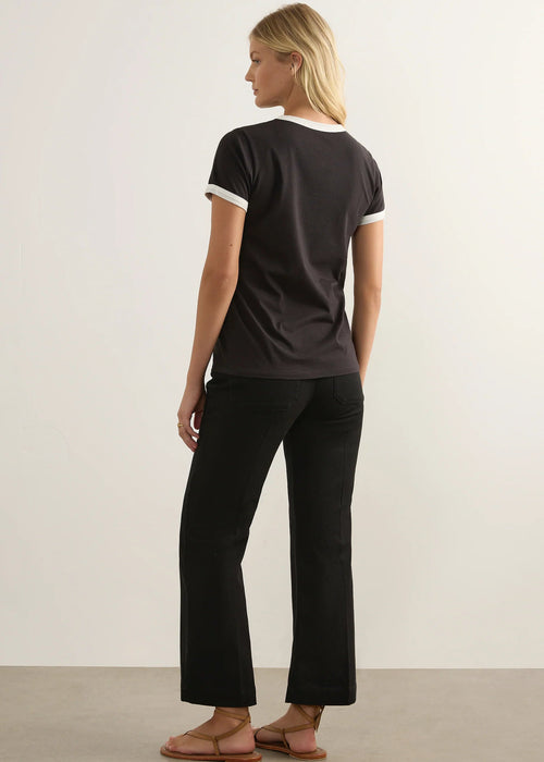 A blonde woman modelling a black ringer T-shirt with white trim on the crew neck and sleeve cuffs, featuring a left chest pocket with a small white embroidered logo.