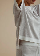 A woman wearing a light grey textured knit top and matching skirt against a solid beige background.