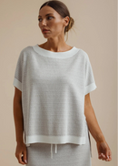 A woman wearing a light grey textured knit top and matching skirt against a solid beige background.