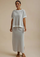 A woman wearing a light grey textured knit top and matching skirt against a solid beige background.