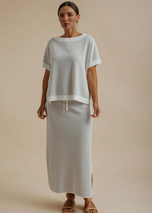 A woman wearing a light grey textured knit top and matching skirt against a solid beige background.