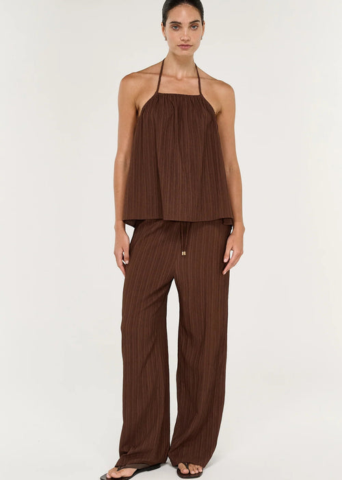 A woman modelling a matching brown two-piece set consisting of a halter-neck top and wide-leg trousers, both featuring a vertical pleated texture, against a plain light background.