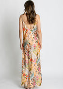 A woman modelling a long spaghetti-strap maxi dress with a multicolour collage print of vintage postcards, flowers, and illustrations, set against a plain light grey studio background.