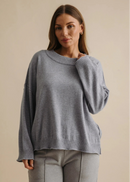 Woman wearing a grey sweater and pants against a beige background