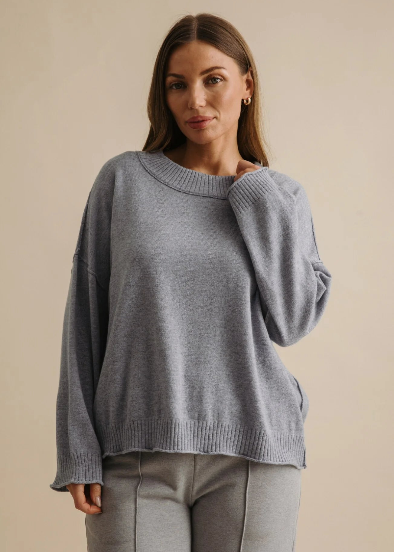 Woman wearing a grey sweater and pants against a beige background