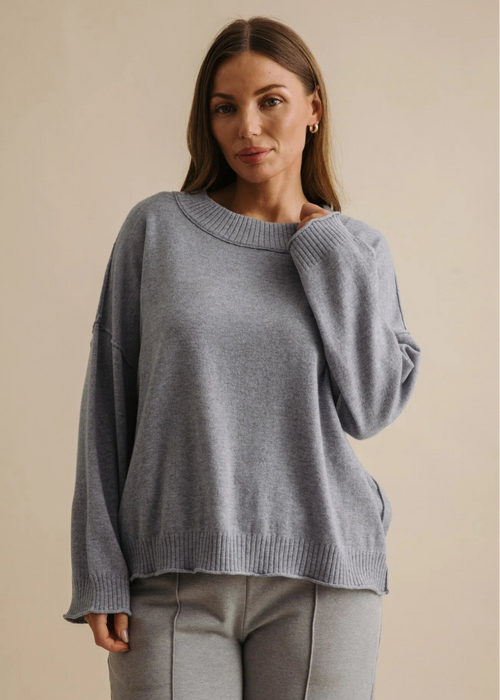 Woman wearing a grey sweater and pants against a beige background