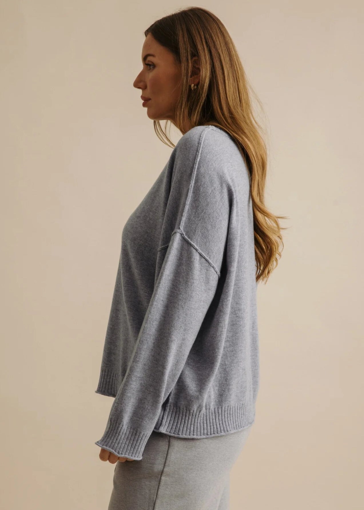 Woman wearing a grey sweater and pants against a beige background