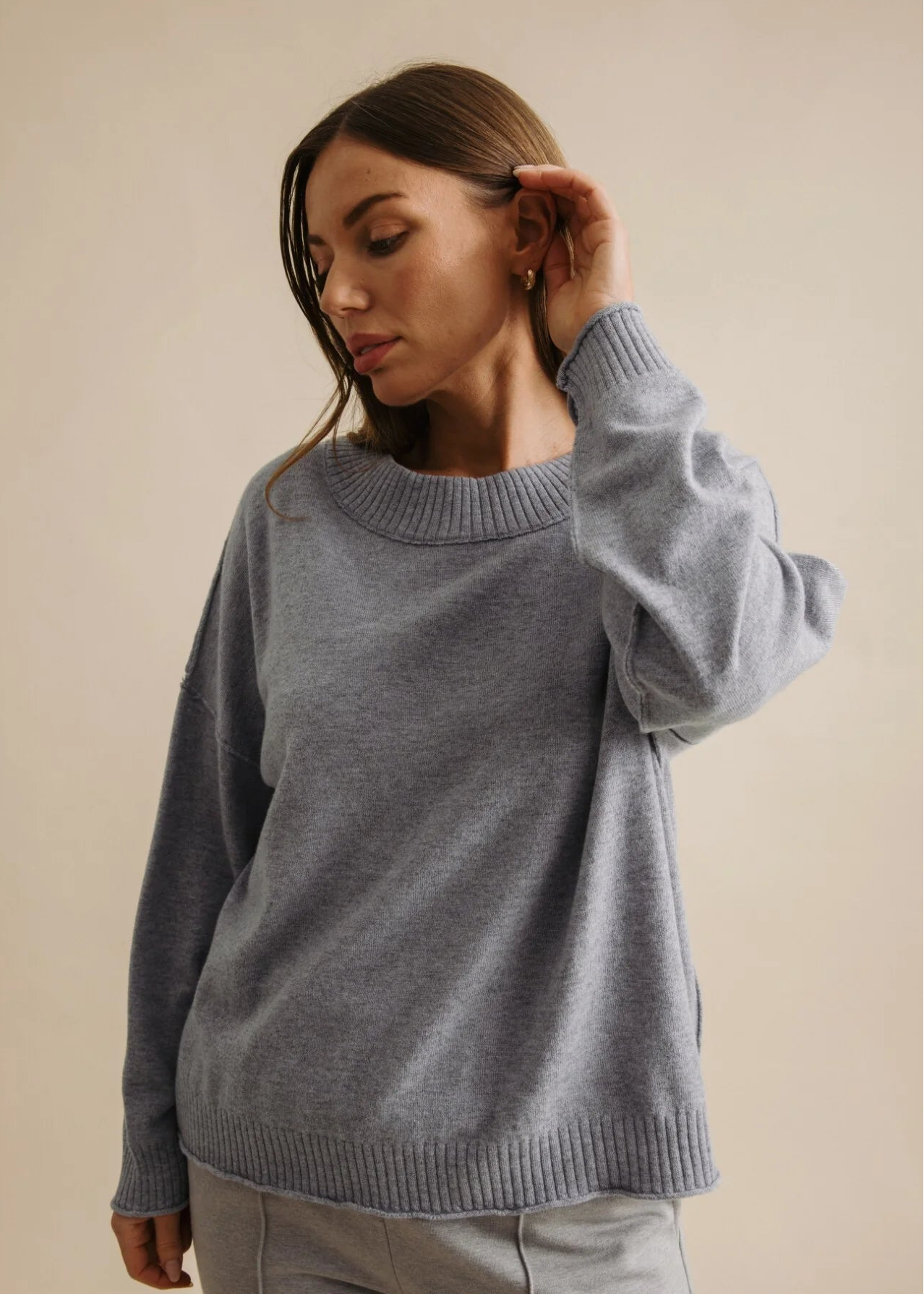 Woman wearing a grey sweater and pants against a beige background