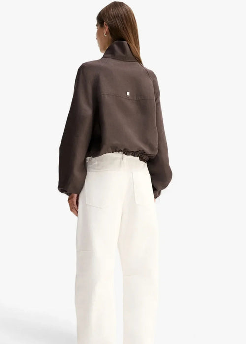 A woman shown from the back wearing a dark brown cropped long-sleeve shirt and white wide-leg trousers, photographed against a clean white studio background.