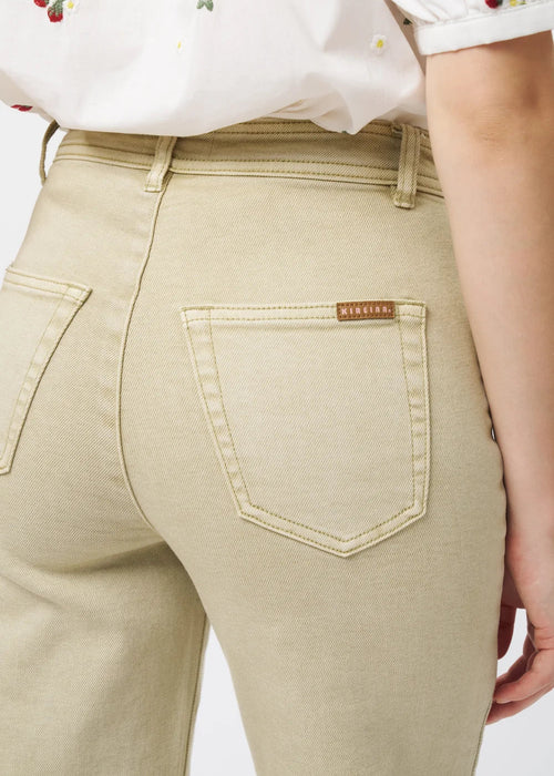 Close-up back view of a person wearing light beige denim jeans with a small brown brand tab on the back pocket, paired with a white floral blouse.