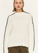 Woman wearing a white sweater with black trim and brown pants on a white background