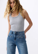 Woman wearing a grey tank top and blue jeans on a white background