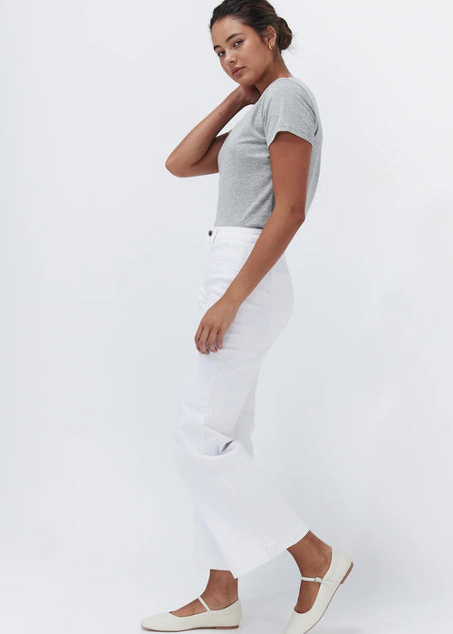 A woman posing in a studio setting, wearing a light grey short-sleeve t-shirt, white wide-leg cropped pants, and off-white flat shoes against a plain white background.