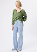 A woman modelling a sage green long-sleeve blouse and light blue wide-leg jeans against a plain white studio background.