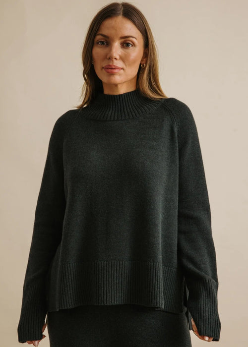 Woman wearing a dark green sweater against a beige background