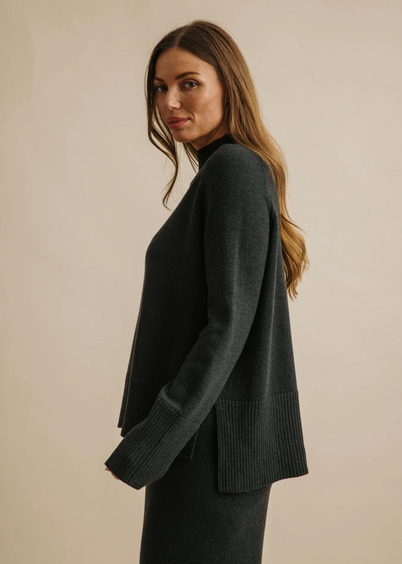 Woman wearing a dark green sweater against a beige background
