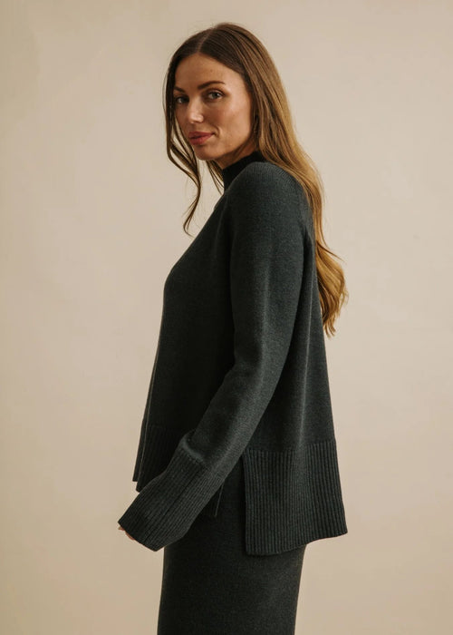 Woman wearing a dark green sweater against a beige background