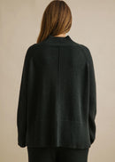 Woman wearing a dark green sweater against a beige background
