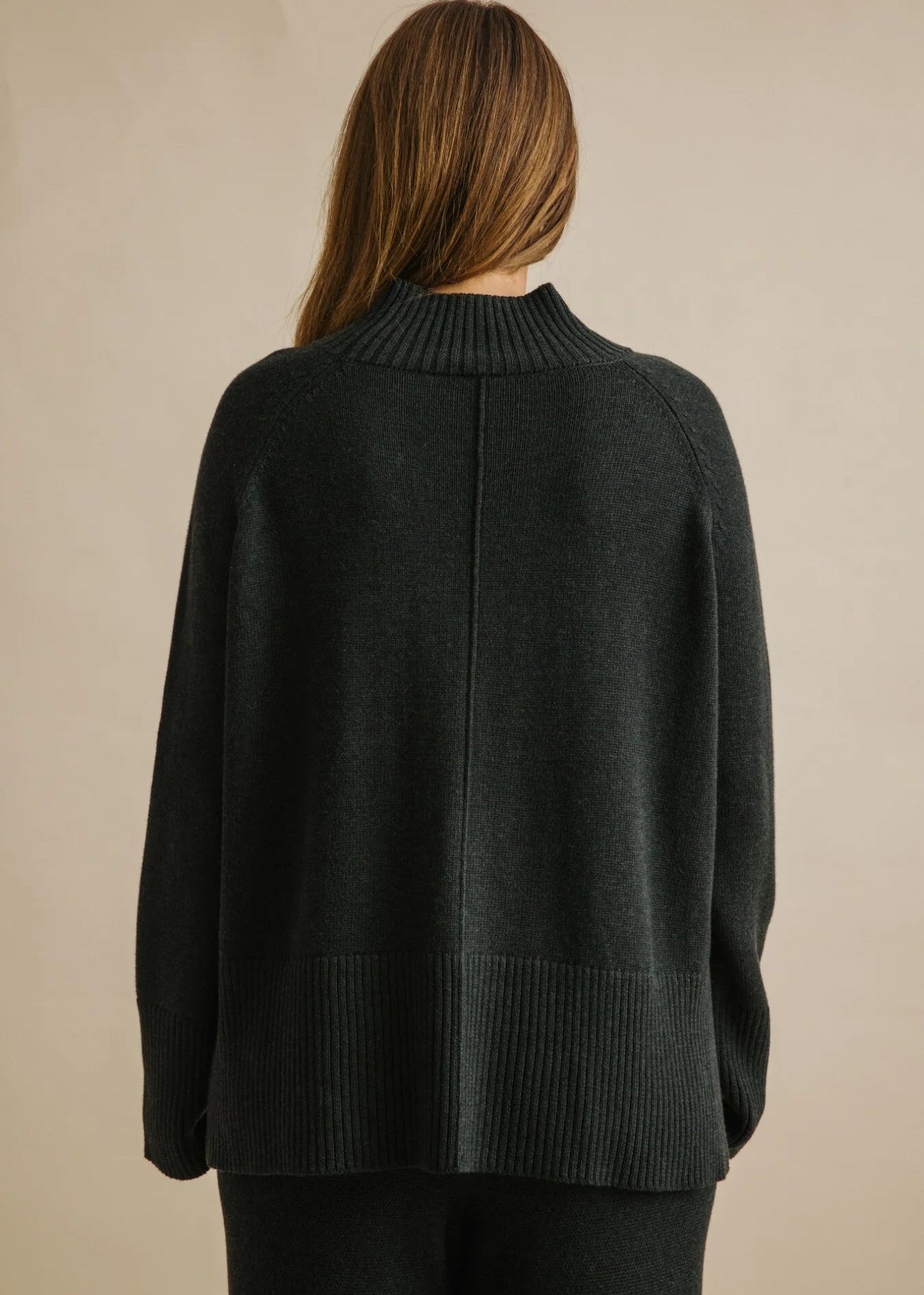Woman wearing a dark green sweater against a beige background