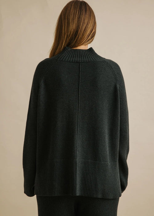 Woman wearing a dark green sweater against a beige background
