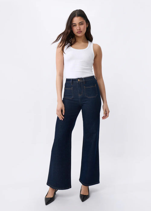 Woman wearing dark blue flared jeans and a white top on a white background