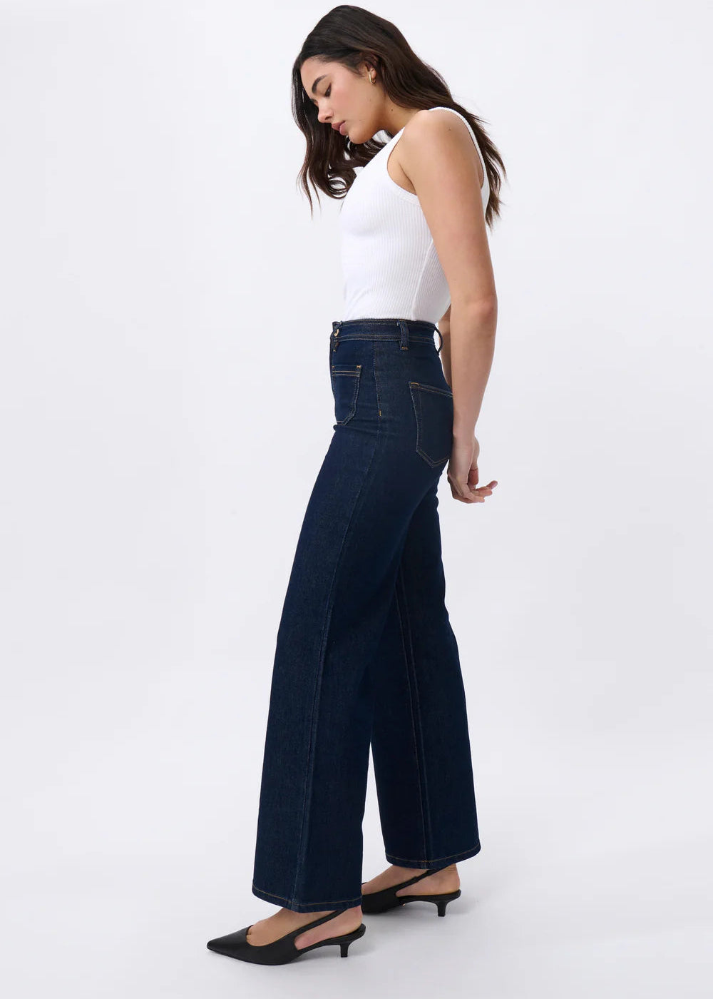 Woman wearing dark blue flared jeans and a white top on a white background