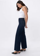 Woman wearing dark blue flared jeans and a white top on a white background