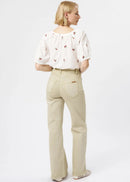 A woman is shown from the back wearing a white puff-sleeve blouse with small red floral embroidery and beige straight-leg jeans, photographed against a clean white studio background.