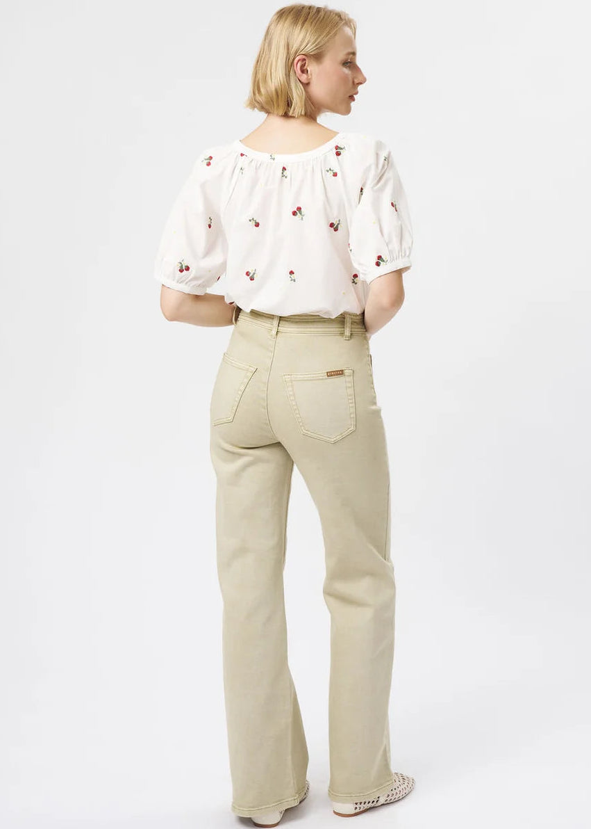 A woman is shown from the back wearing a white puff-sleeve blouse with small red floral embroidery and beige straight-leg jeans, photographed against a clean white studio background.