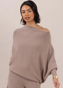 Woman wearing a beige off-shoulder top and pants against a plain background
