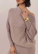Woman wearing a beige off-shoulder top and pants against a plain background