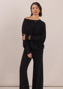 Woman wearing a black off-shoulder sweater and wide-leg pants on a beige background