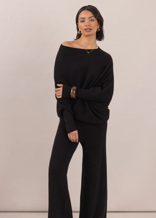 Woman wearing a black off-shoulder sweater and wide-leg pants on a beige background