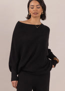Woman wearing a black sweater and pants against a beige background