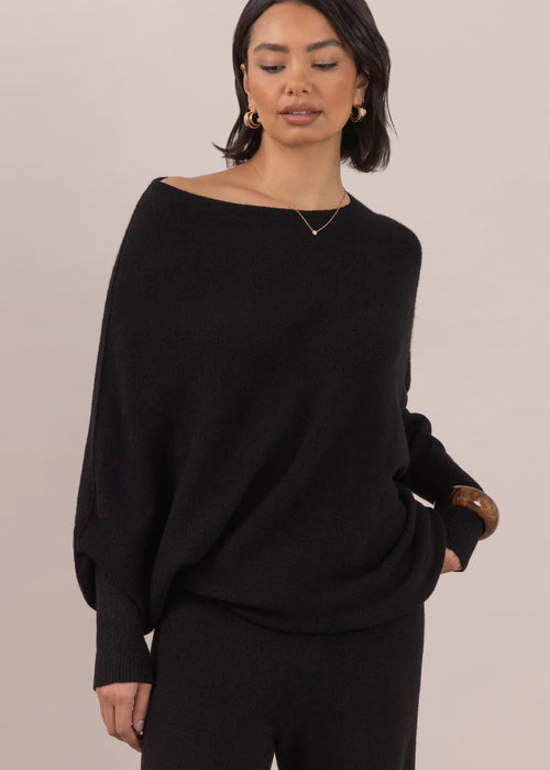 Woman wearing a black sweater and pants against a beige background