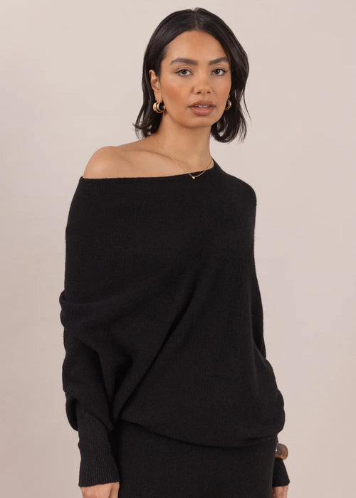 Woman wearing a black off-shoulder top and pants on a beige background
